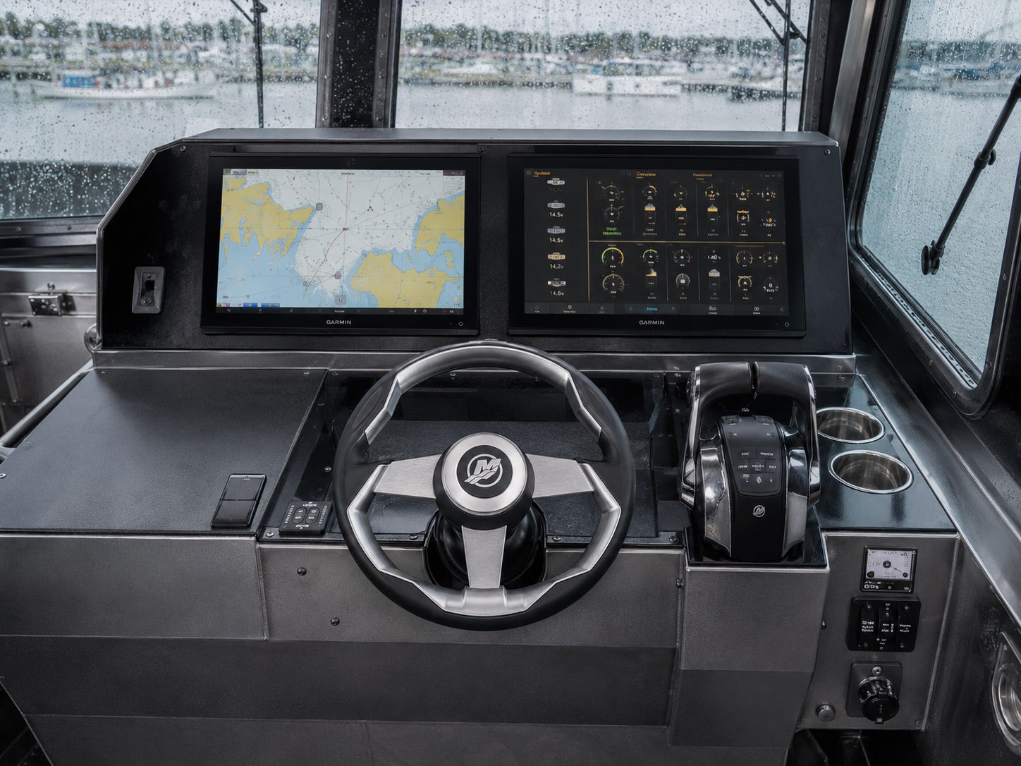 LC-259 M.U.L.E. helm with twin Garmin chartplotter and engine-data displays, Mercury steering wheel, and joystick throttle controls, viewed through rain-streaked pilothouse windows.