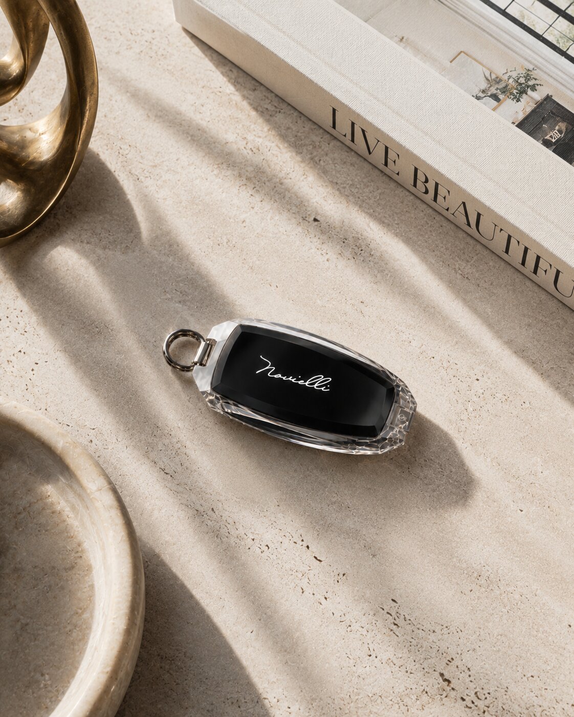 Crystal Novielli key fob with engraved script resting on a travertine surface beside a design book.