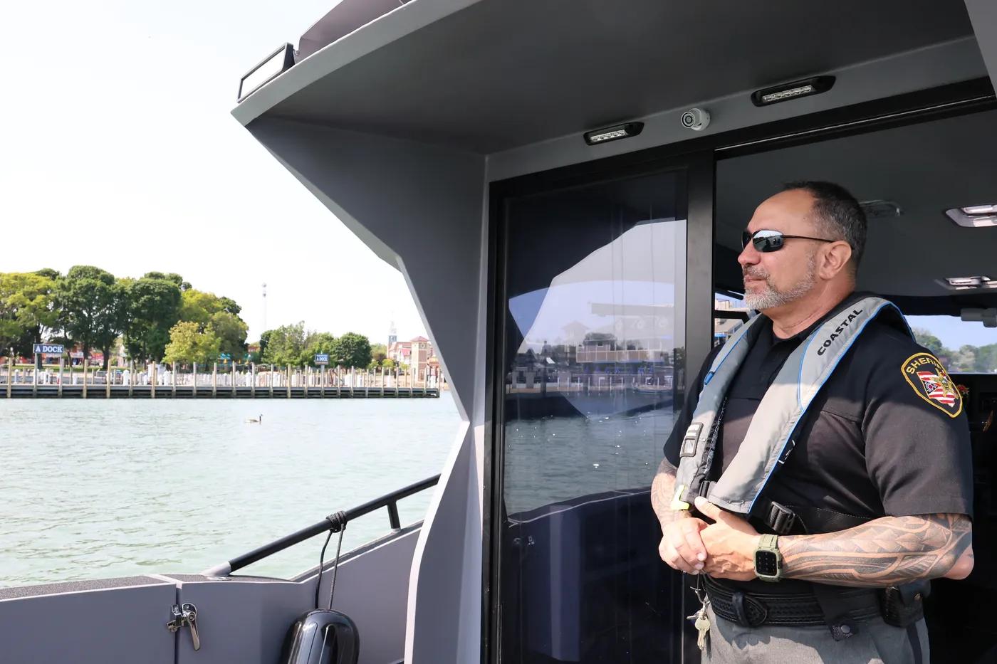 Sheriff's deputy in a coastal life vest standing aboard a Novielli patrol vessel near a waterfront.