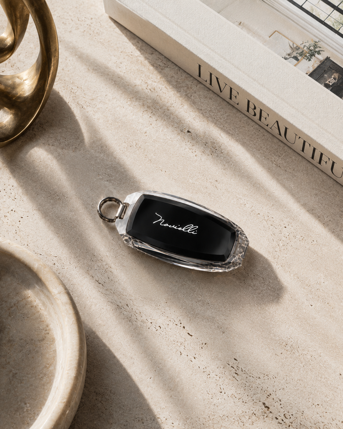 Crystal Novielli key fob with engraved script resting on a travertine surface beside a design book.