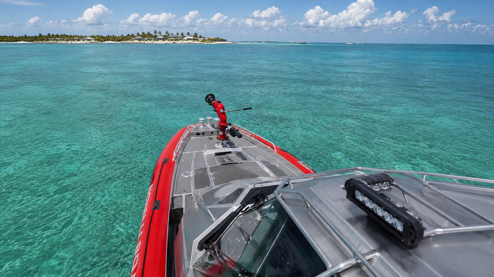 Bow view of the Inferno 299 Fire Rescue with red fire monitor mounted forward, idling on turquoise tropical water with a palm-lined island in the distance.