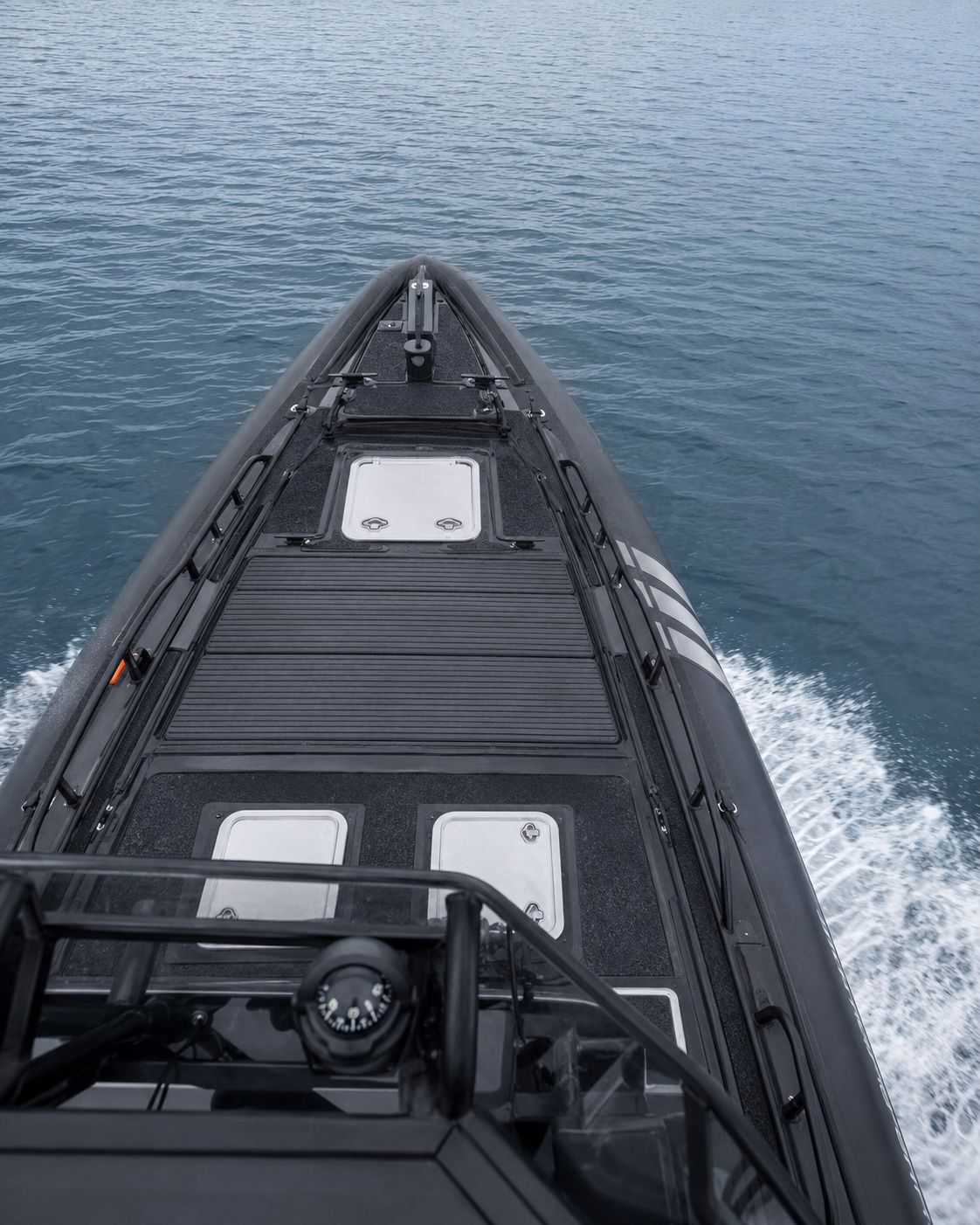 Aerial view from the hardtop looking down the blacked-out bow of the Revenant 369 Blackline SAR underway, cutting a clean wake across deep blue water.