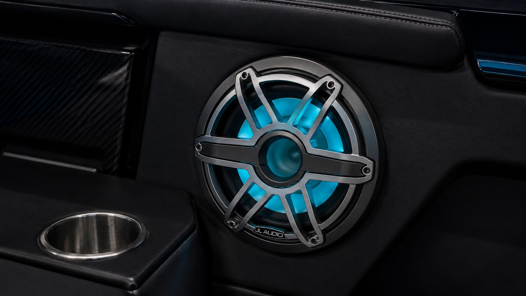 Close-up of a JL Audio marine speaker with blue accent lighting set into the Outlaw 559 LR cabin trim panel beside a stainless cup holder.