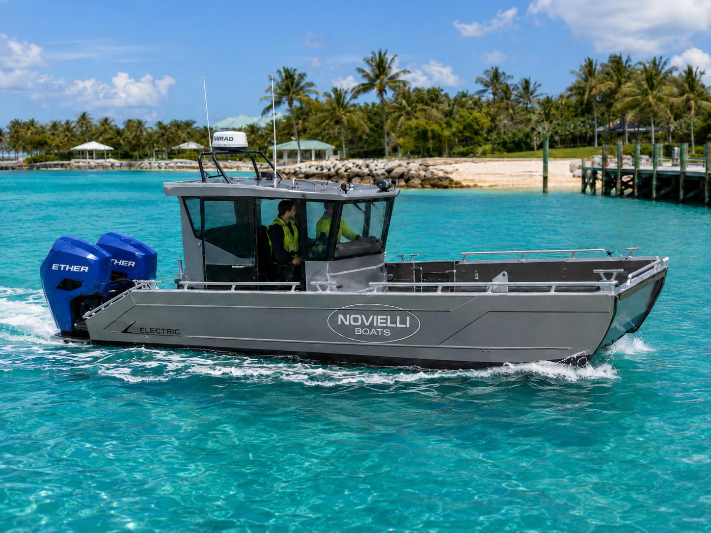 Novielli aluminum electric landing craft with pilothouse and twin blue Ether electric outboards underway on turquoise water past a palm-lined tropical shoreline, crewed by operators in high-visibility vests.